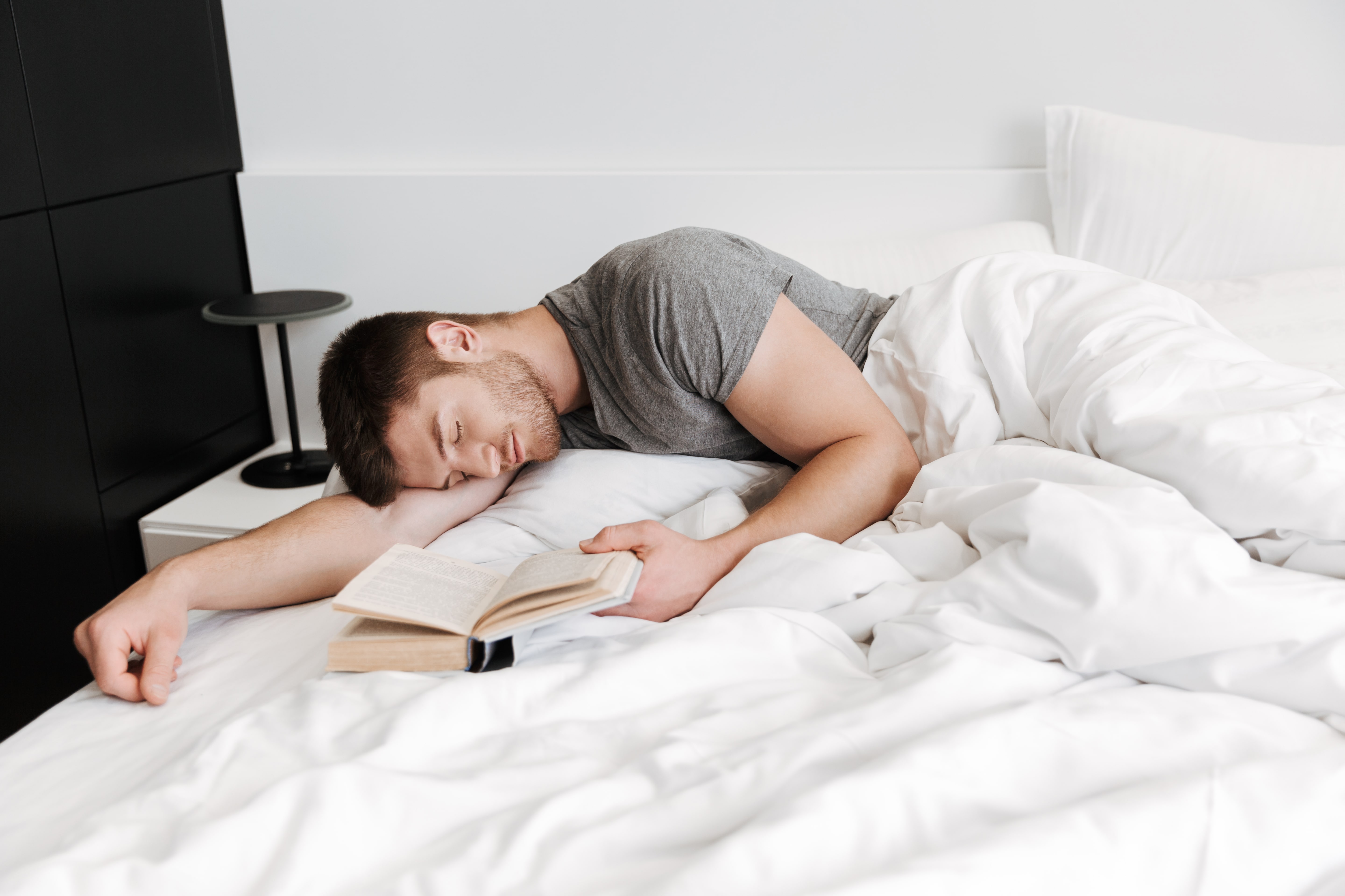 Nauka podczas snu - śpiący mężczyzna z książką w łóżku.