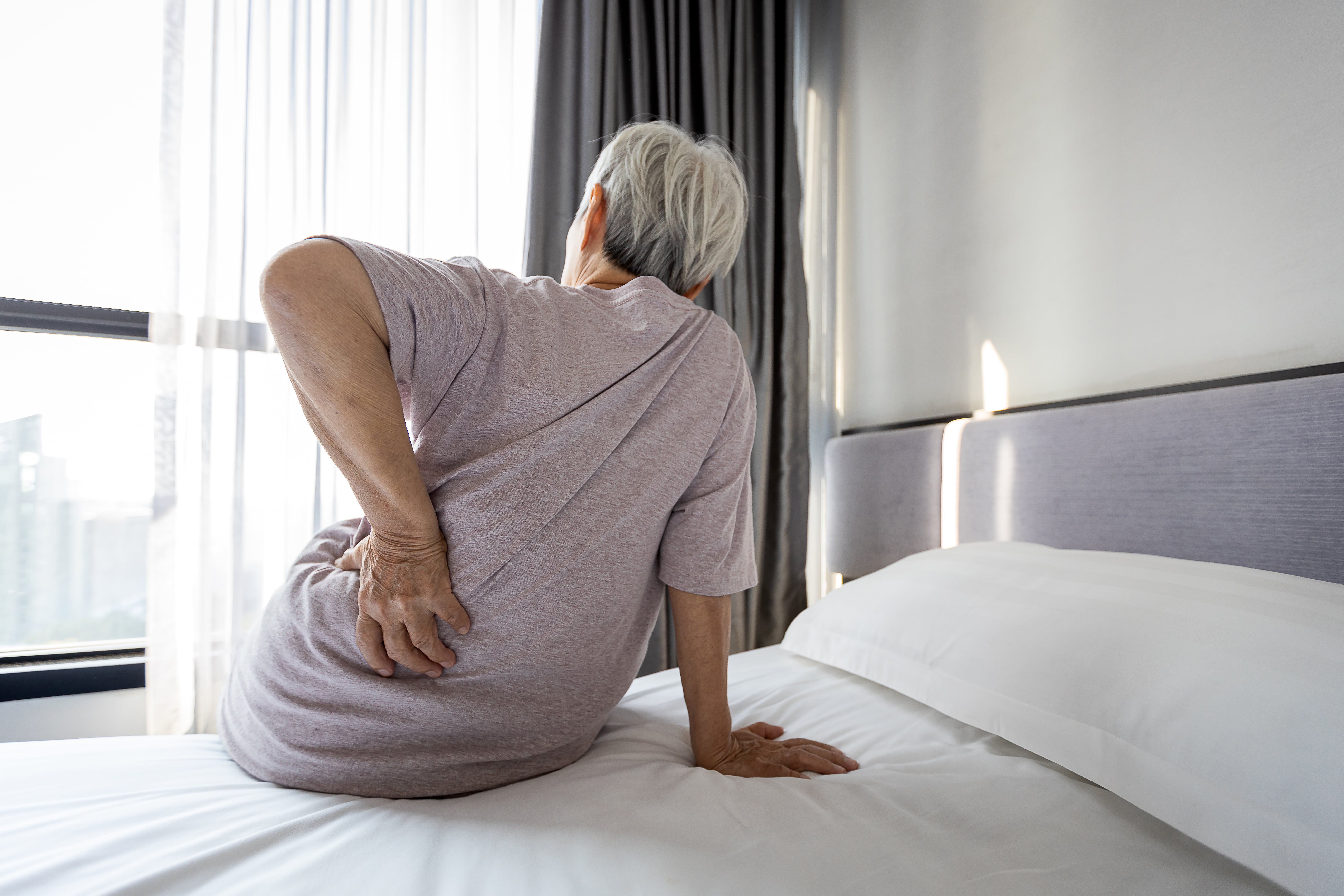 Starsza kobieta z bólem pleców siedzi na łóżku
